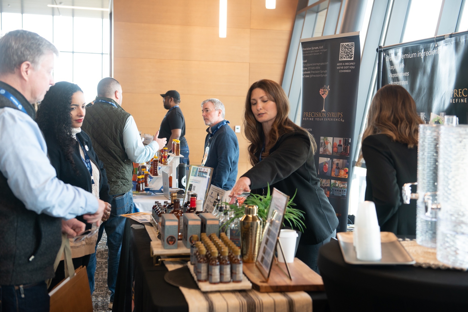 People interacting at a syrup vendor's table during an indoor event