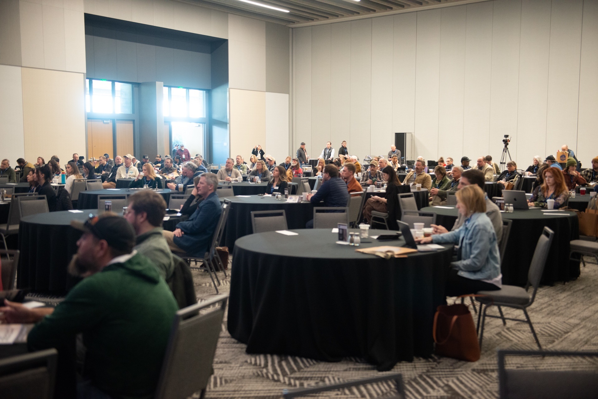 Attendees seated at round tables during a conference in a large, well-lit room