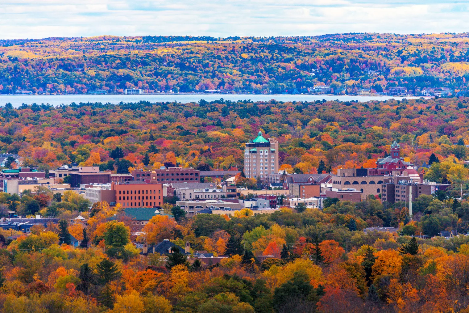 A landscape photo of a lake and fall-colored trees surrounding a town.